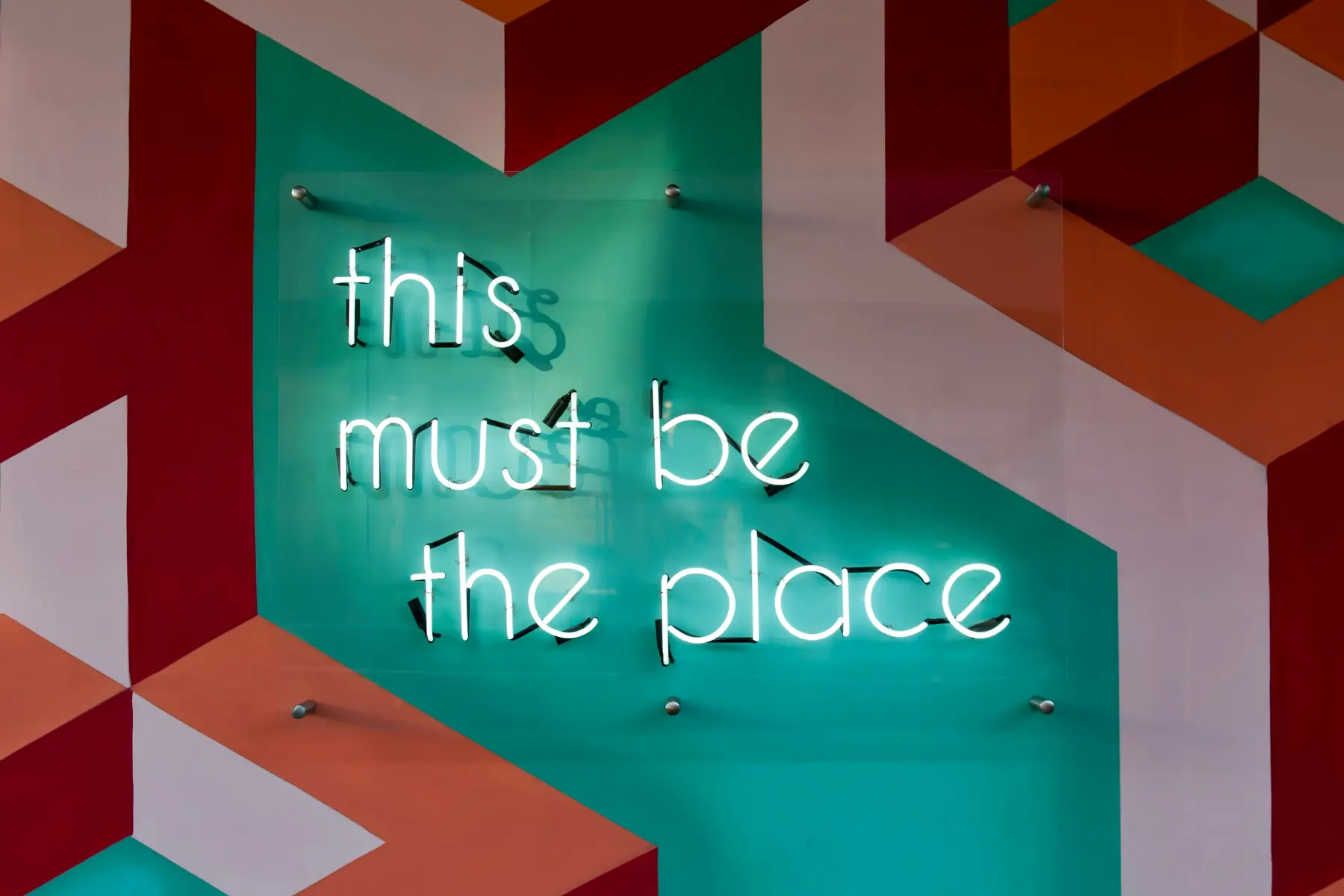 Neon sign reading “this must be the place” on a colourful graphic wall, symbol of an employer brand that makes people want to join the company